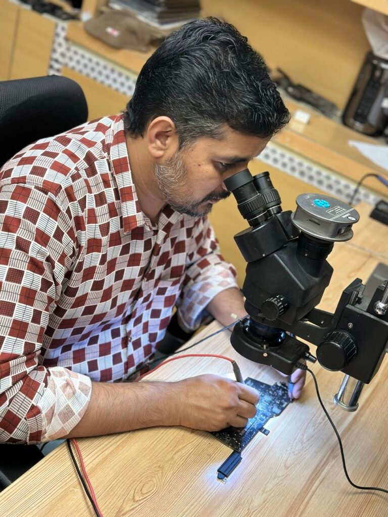 Mak Doctor technician repairing a MacBook logic board under a microscope in Riyadh